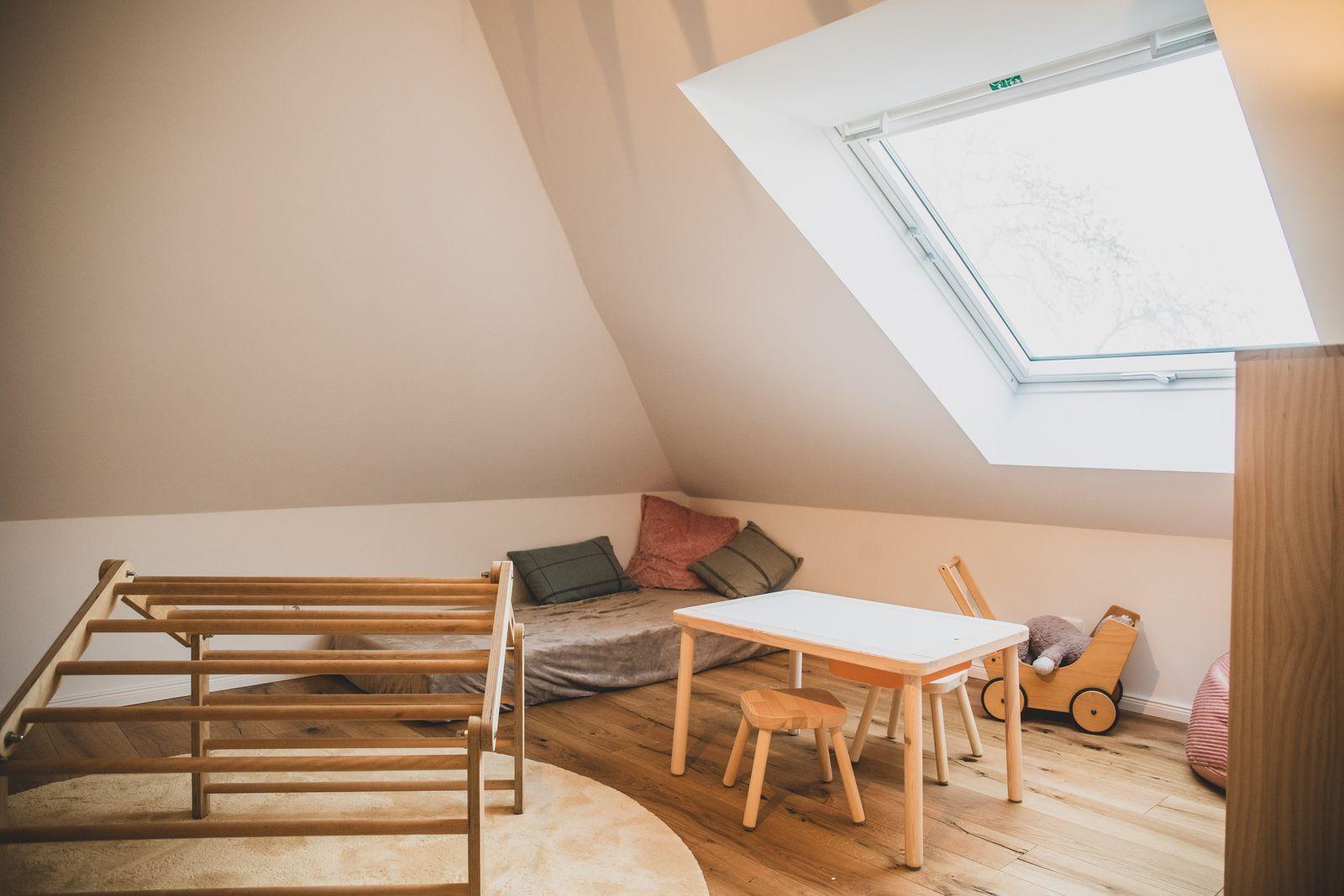 Dachgeschosszimmer mit Holzboden, Dachfenster, Kindertisch, Stühlen und Spielzeug.