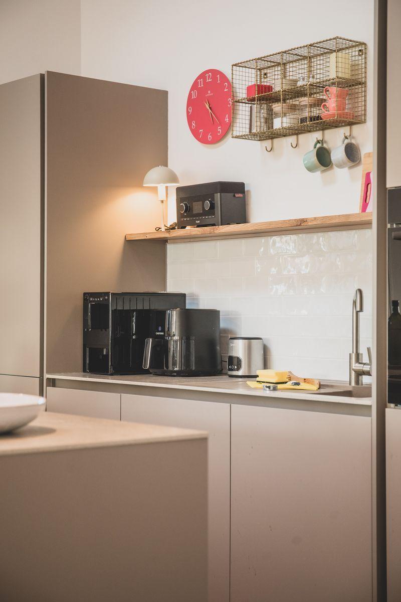 Küche mit Kaffeemaschine, Wanduhr und Aufbewahrungskörben.