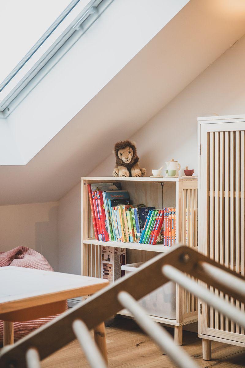 Dachgeschosszimmer mit Bücherregal, Spielzeuglöwe und Dachfenster.