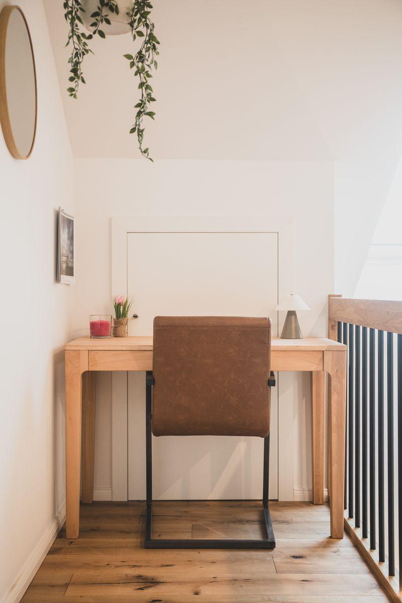 Ein Schreibtisch mit Stuhl, Lampe und Pflanze in einem Raum mit Holzboden und hohem Dach.