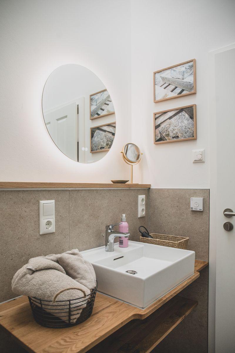 Badezimmer mit runden Spiegel, Waschbecken und dekorativen Bildern an der Wand.