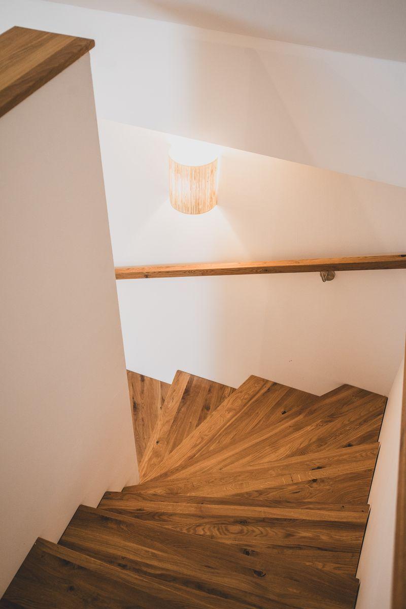 Holzgetreppe mit Handlauf und Deckenleuchte in einem hellen Raum.
