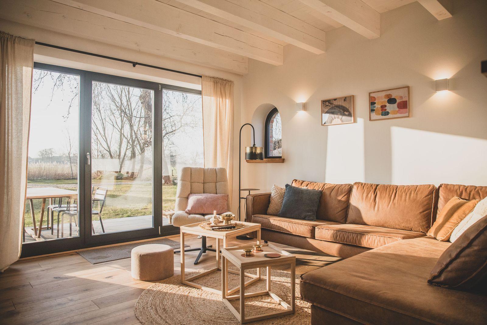 Wohnzimmer mit braunem Sofa, Holzboden und großem Fenster zur Terrasse.