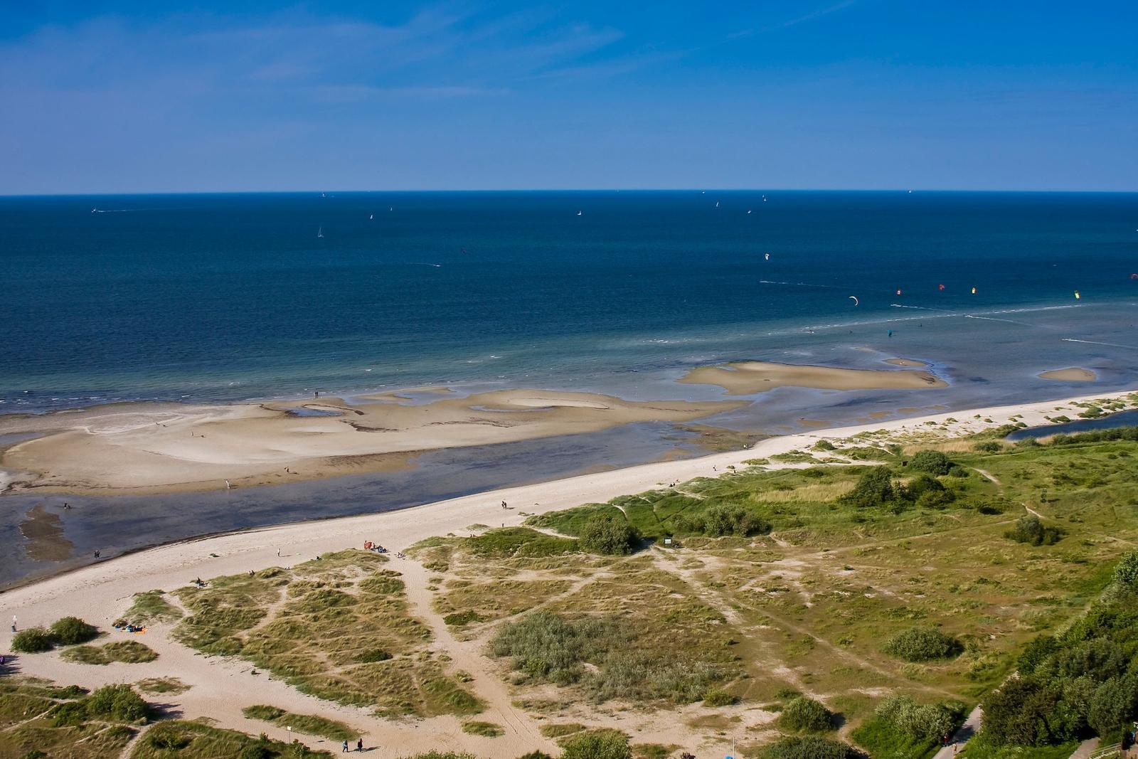 Strand mit Dünen und Meer, Segelboote und Kitesurfer im Hintergrund.