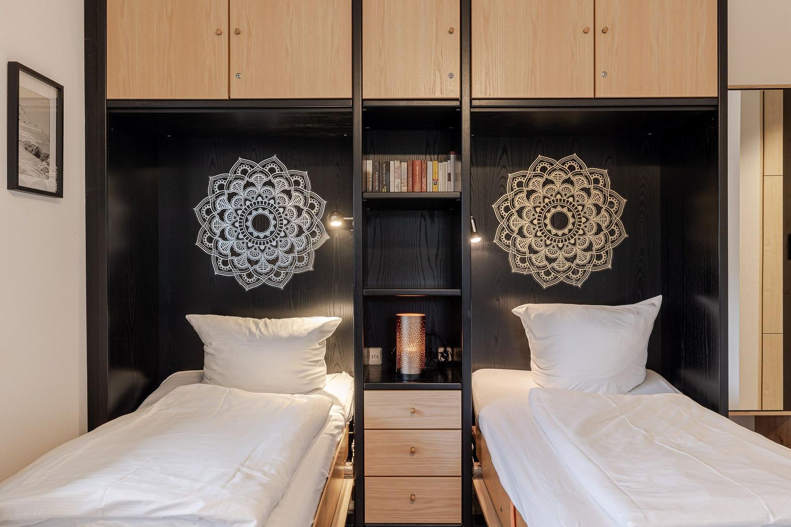 Two beds with white bedding, black walls with mandala motifs and wooden shelves.