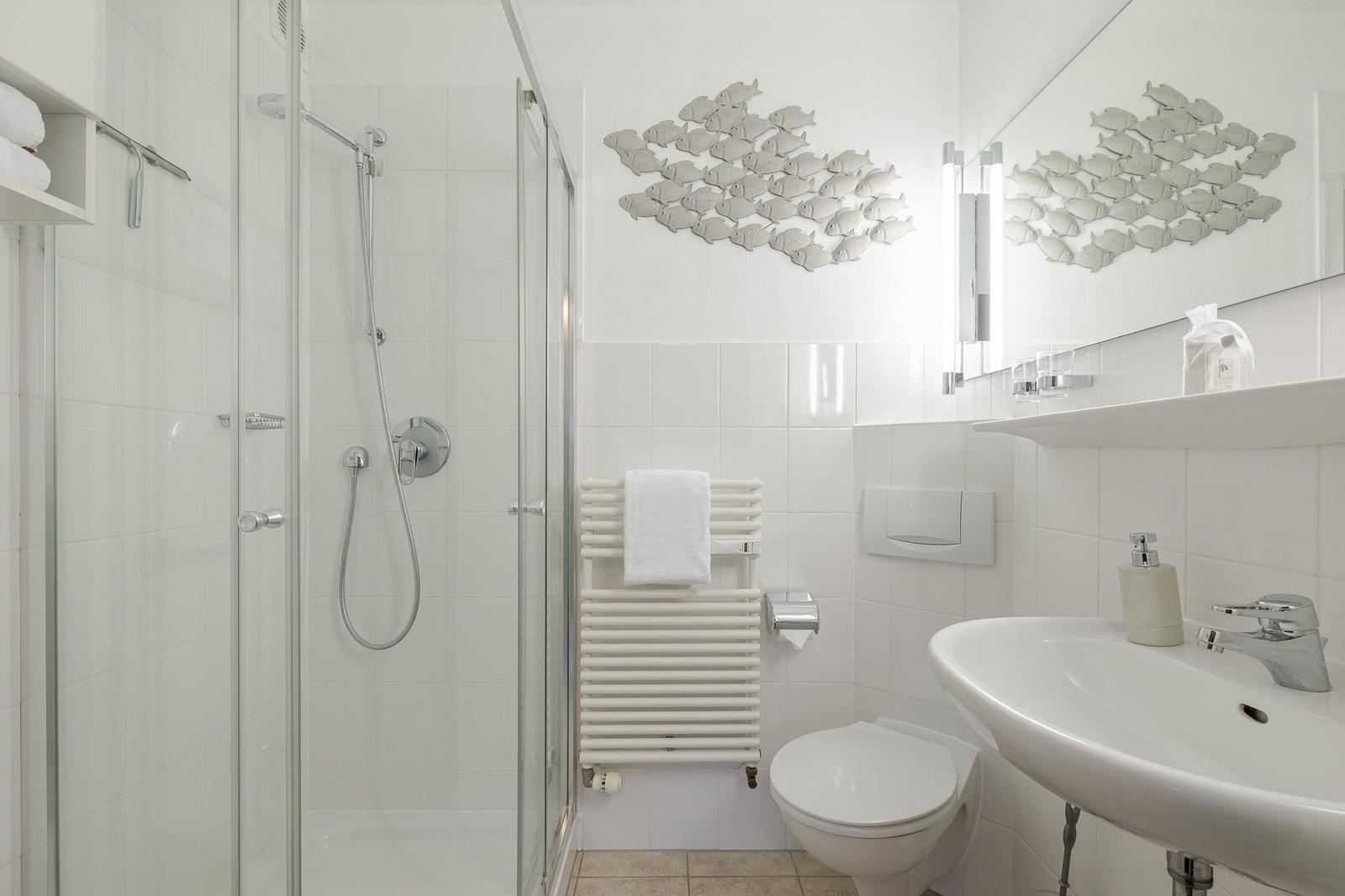 Bathroom with shower, toilet, and sink. Wall decoration of fish.