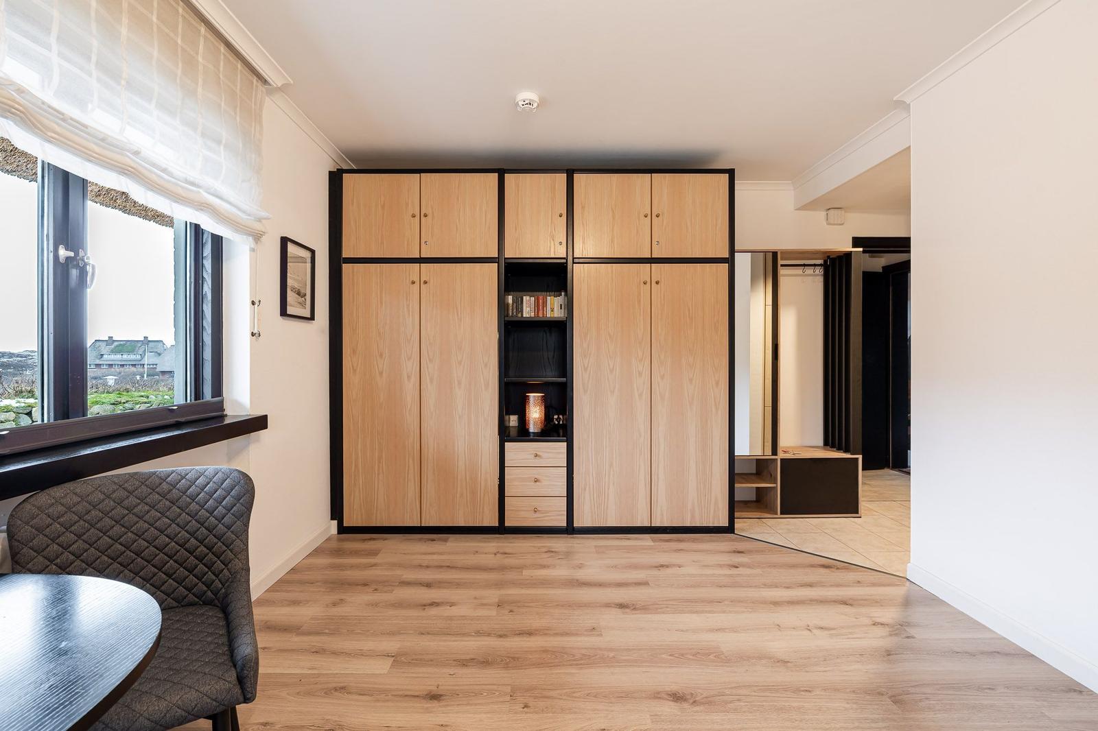 Bedroom with wooden closet, window, and chair. View of outdoor area.