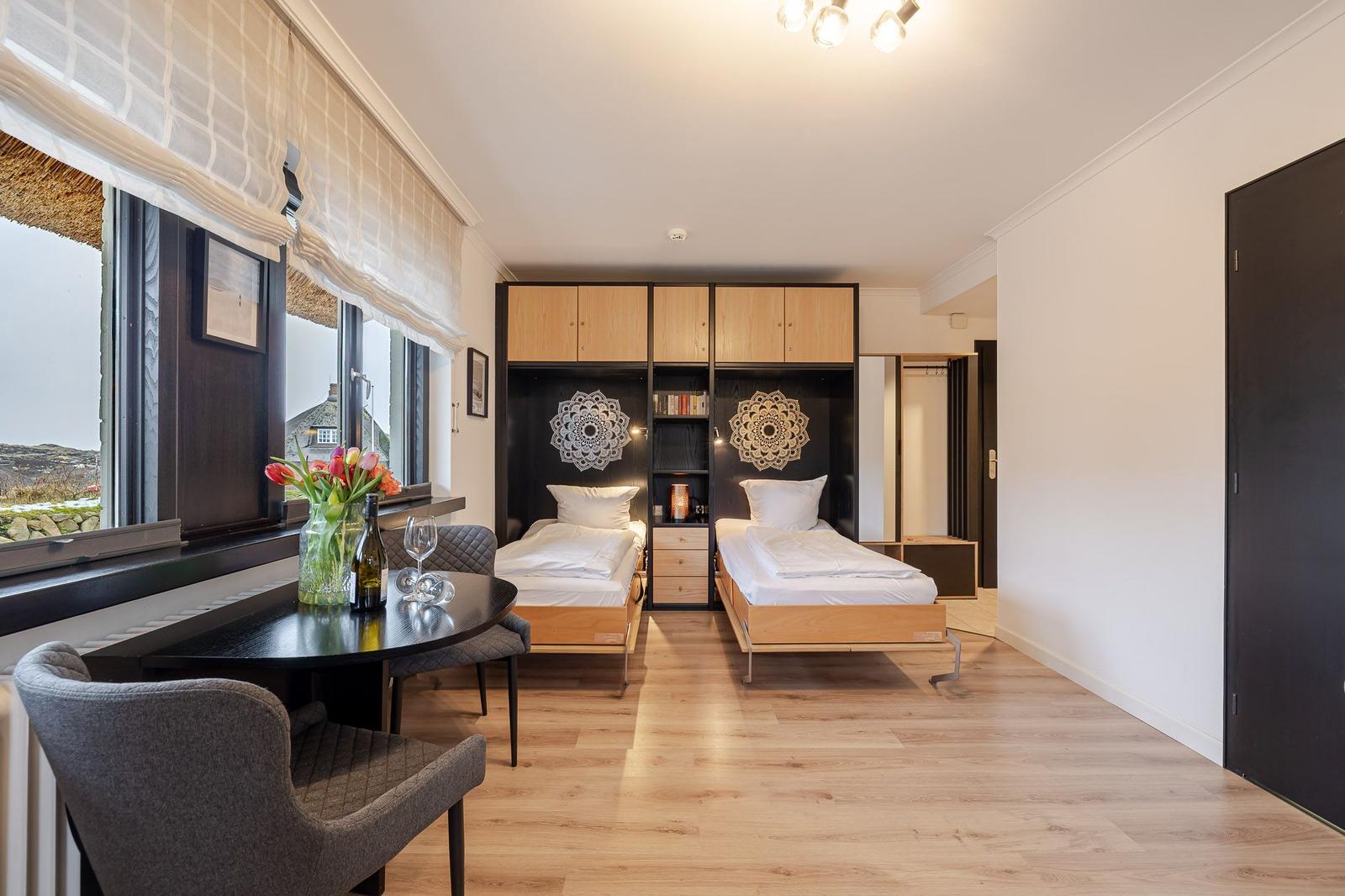 Two beds, table with chairs, window view. Wooden floor and cabinets.