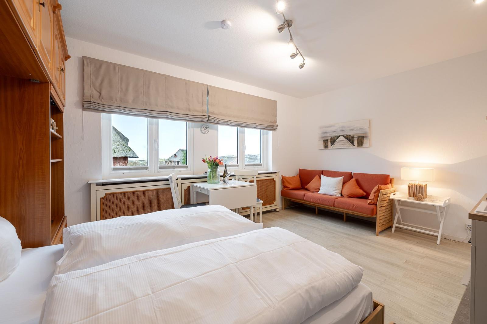 Zimmer mit Doppelbett, Sofa und Fensterblick auf Dächer.