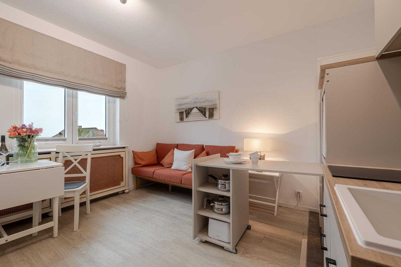 Wohnküche mit Sofa, Tisch und Fenster. Küchenzeile mit Spüle und Arbeitsfläche.