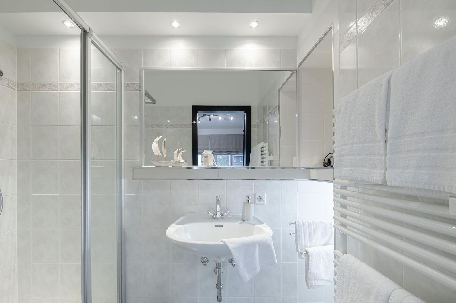 Badezimmer mit Dusche, Waschbecken und Handtuchhalter. Spiegel und Segelboot-Dekoration.