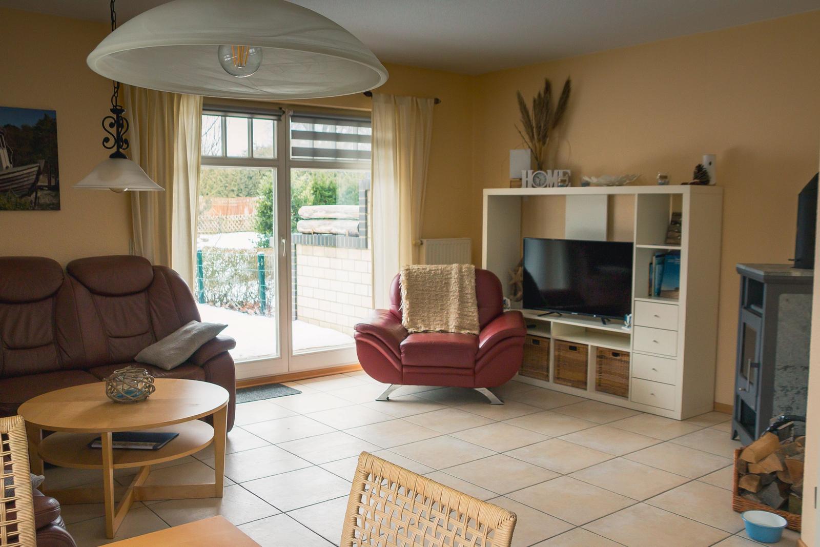 Wohnzimmer mit Sofa, Sessel, TV und Terrassentür.
