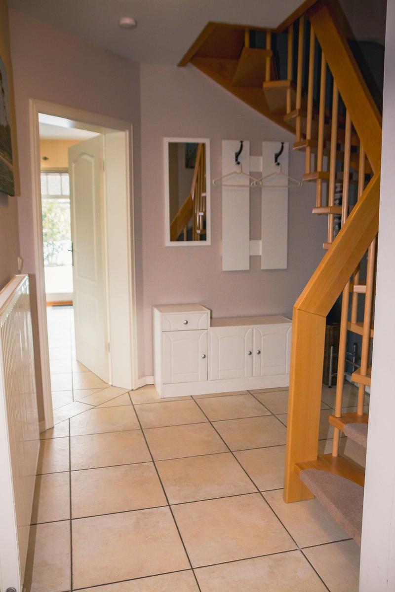 Eingangsbereich mit Holztreppe, weißen Schuhschränken und Spiegel an der Wand.
