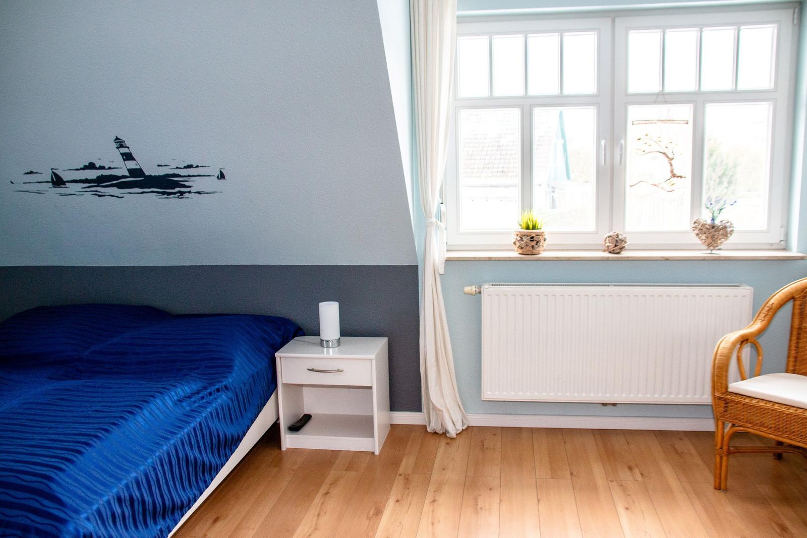 Schlafzimmer mit Bett, Nachttisch und Fenster. Wanddekoration mit Leuchtturm.