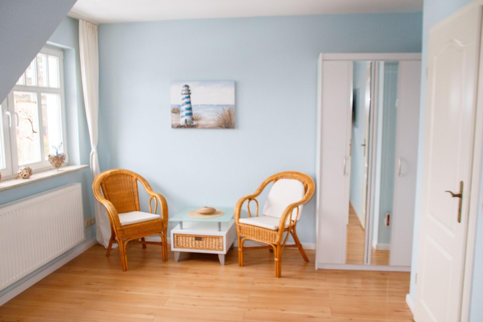 Zimmer mit zwei Stühlen, Tisch und Wandbild eines Leuchtturms.