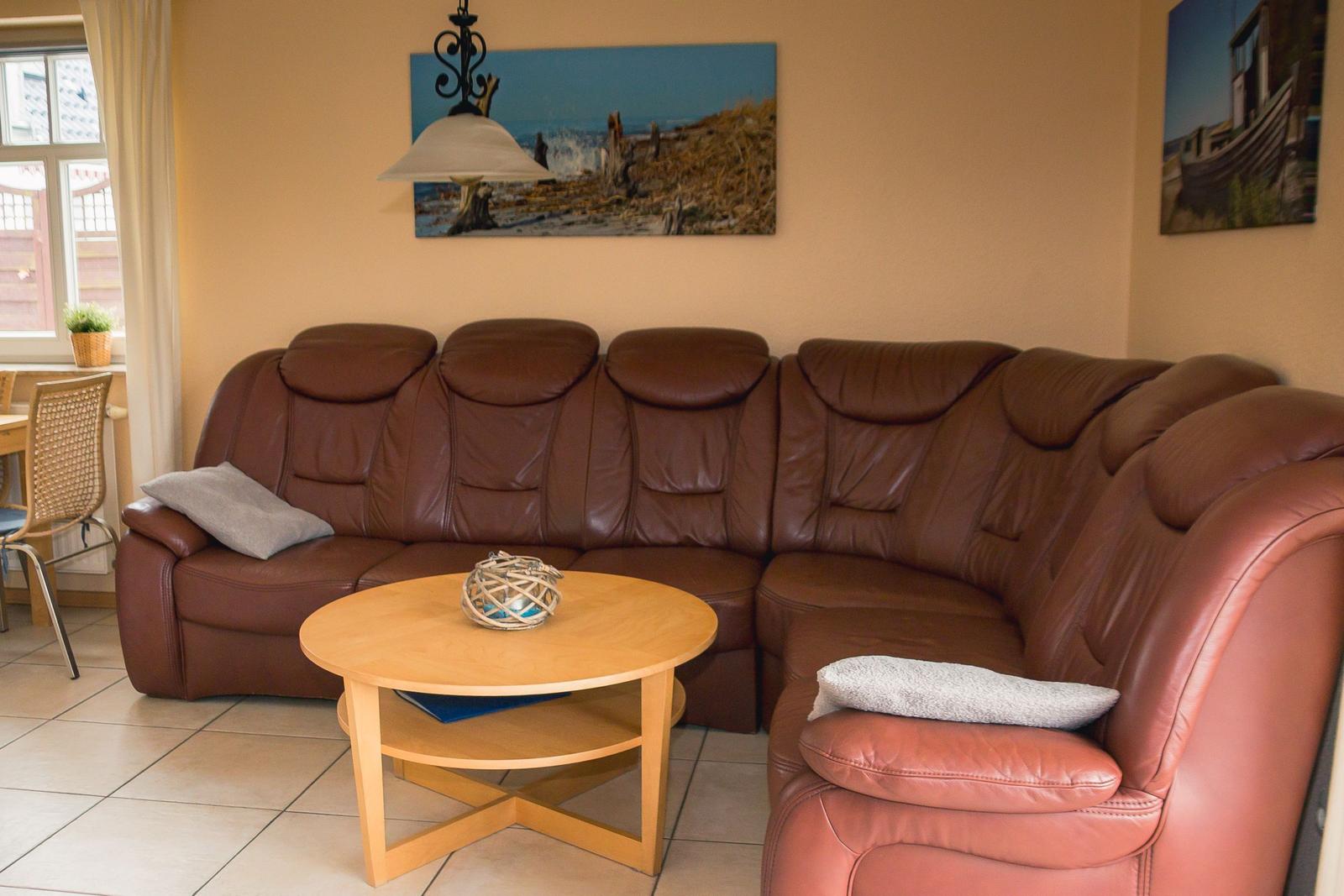 Ein Wohnzimmer mit braunem Sofa, runden Tisch und Wandbildern.