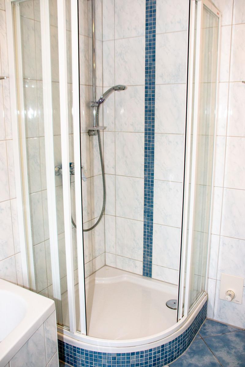 Duschkabine mit Glaswand und blauen Mosaikfliesen an der Wand und Boden.