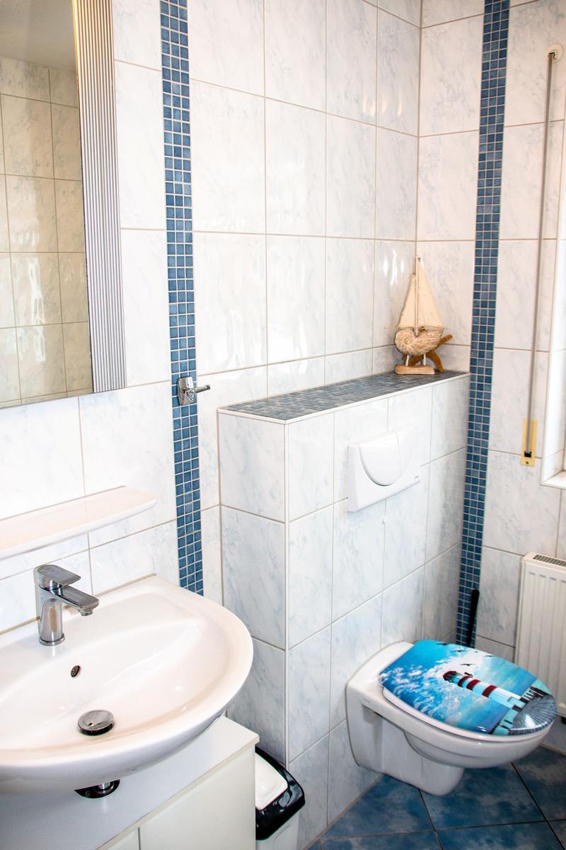 Badezimmer mit Waschbecken, Toilette und Spiegel. Wandfliesen mit blauen Streifen.