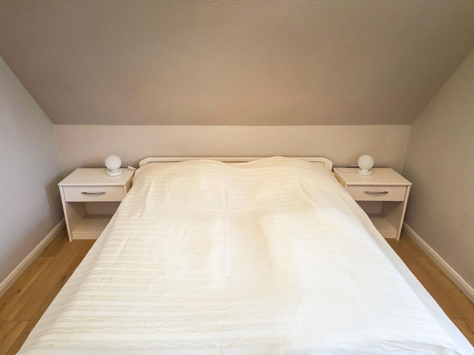 Schlafzimmer mit Doppelbett, zwei Nachttischen und Holzboden unter schrägem Dach.