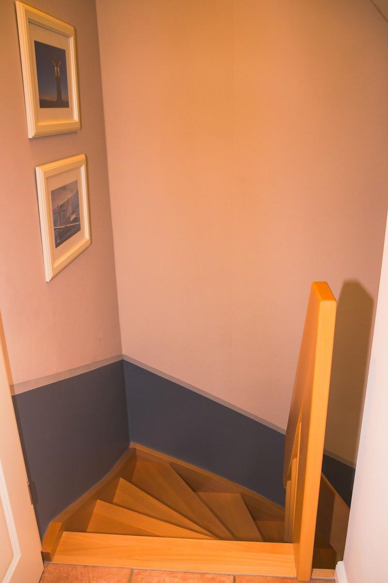 Holztreppe mit Geländer führt nach unten. Wandfarbe cremeweiß und dunkelblau.