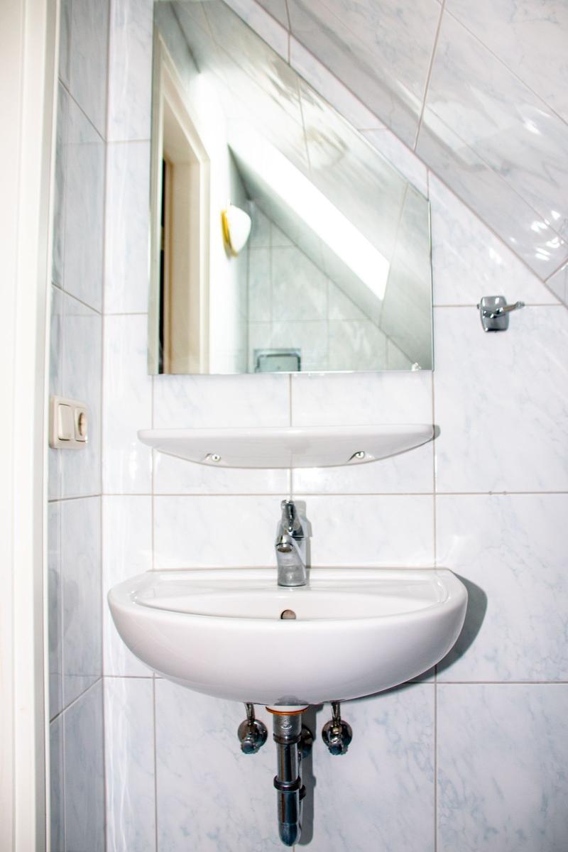 Waschbecken mit Spiegel und Wasserhahn an Wand mit Fliesen