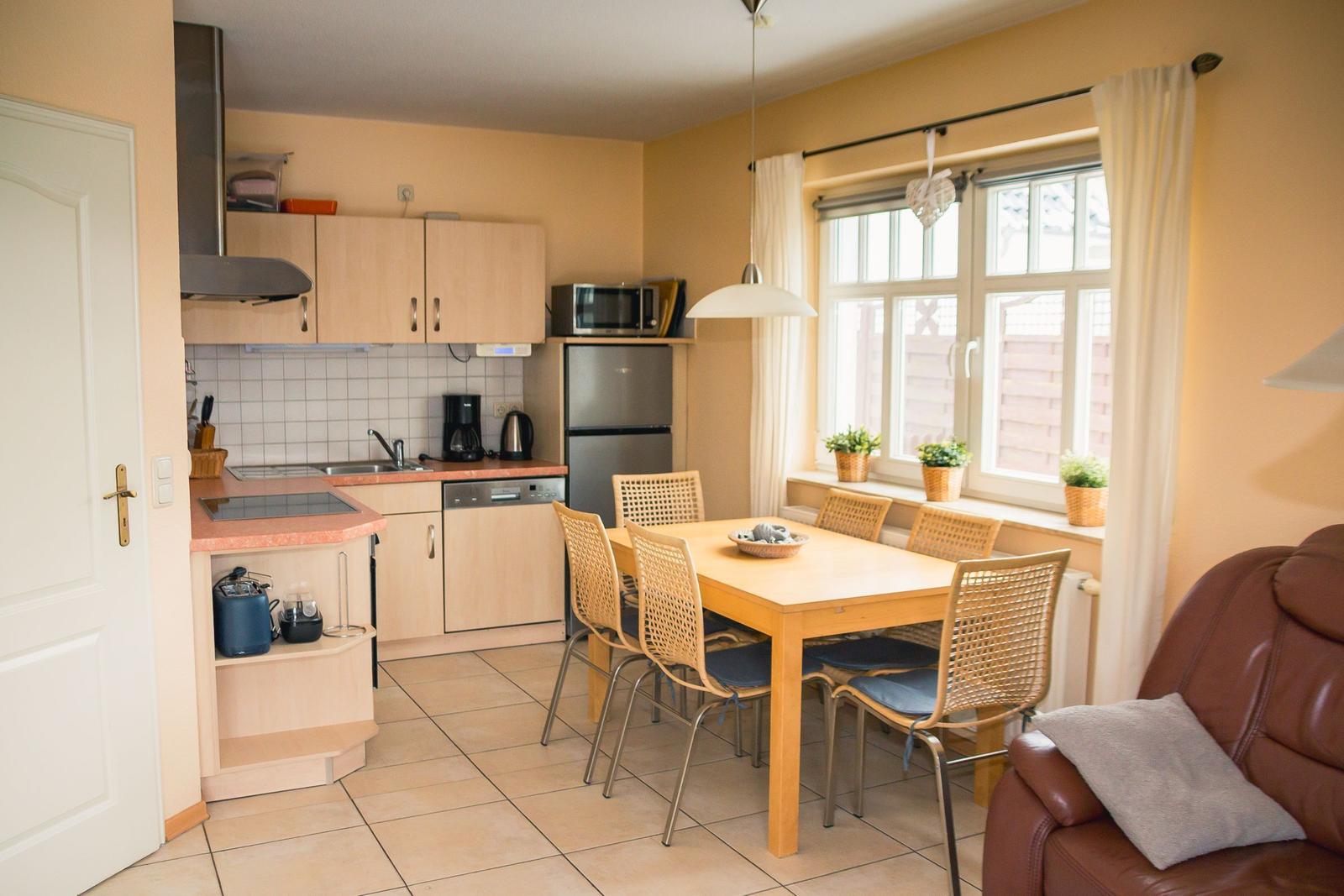 Küche mit Essbereich und Fenster. Holztisch, Stühle, Kühlschrank und Kochfeld.