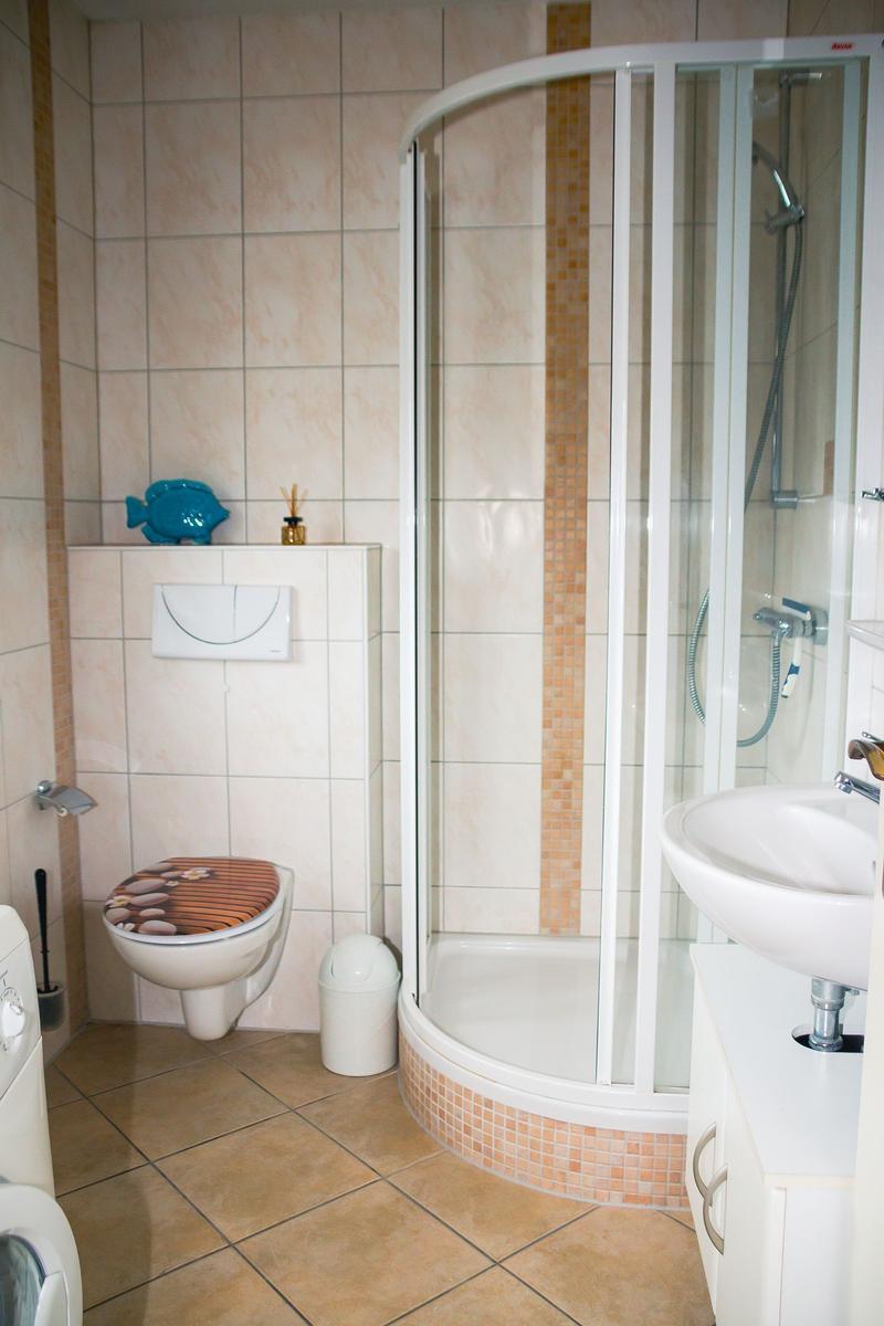 Bad mit Dusche, Waschbecken und Toilette. Fliesen und Mosaik verziert.