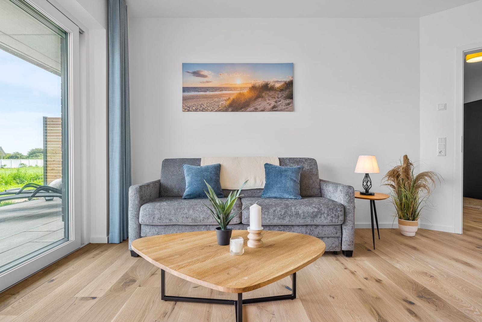 Wohnzimmer mit grauem Sofa, Holztisch und Blick auf Terrasse.