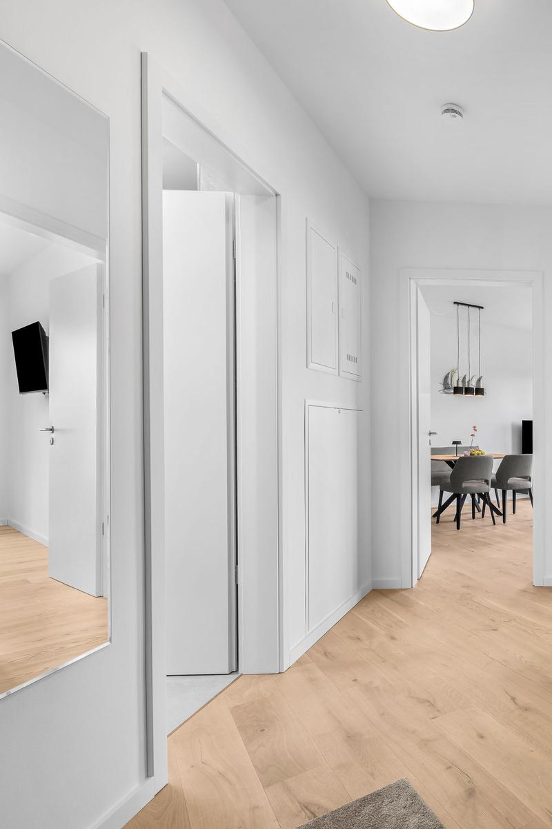 Flur mit weißen Türen und Holzboden, Blick in Esszimmer und Wohnbereich.