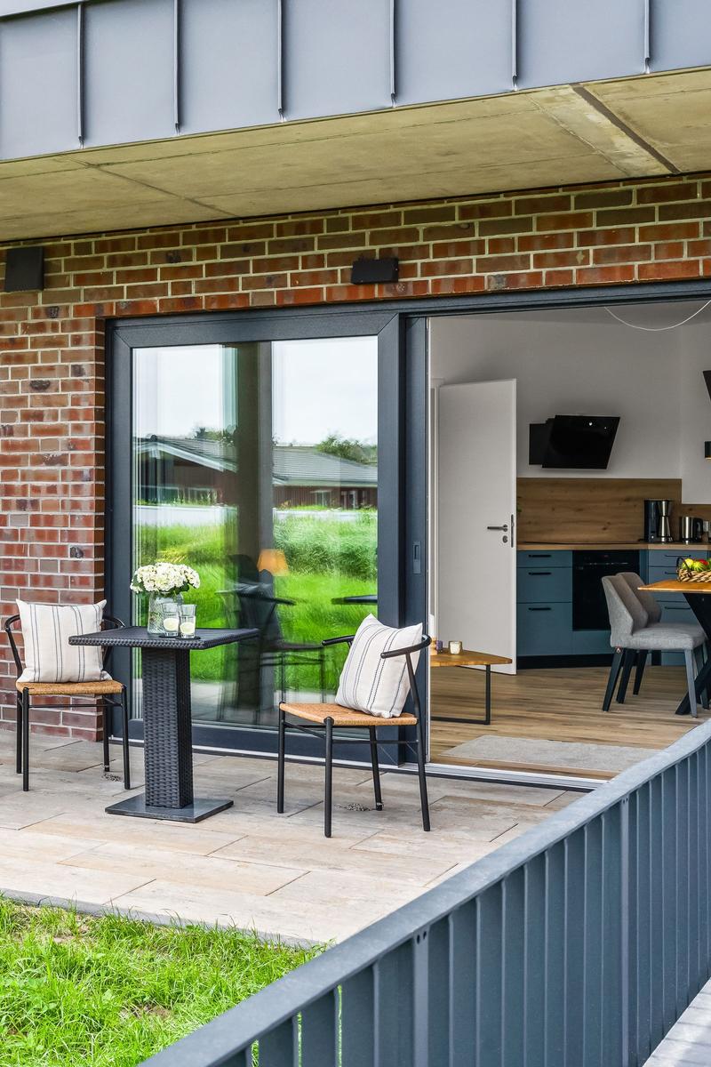 Terrasse mit Tisch und Stühlen, Blick in die Küche mit Holzboden und blauen Schränken.