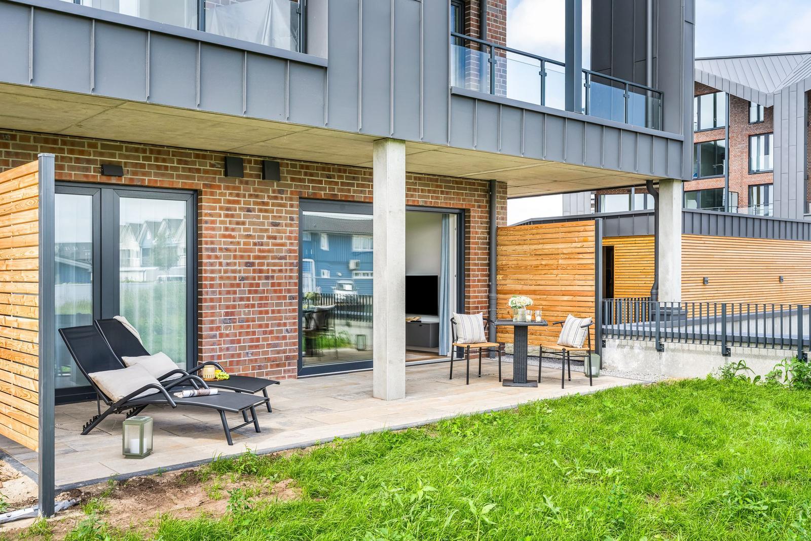 Terrasse mit Liegestühlen und Tisch unter modernem Gebäude mit Backsteinfassade.