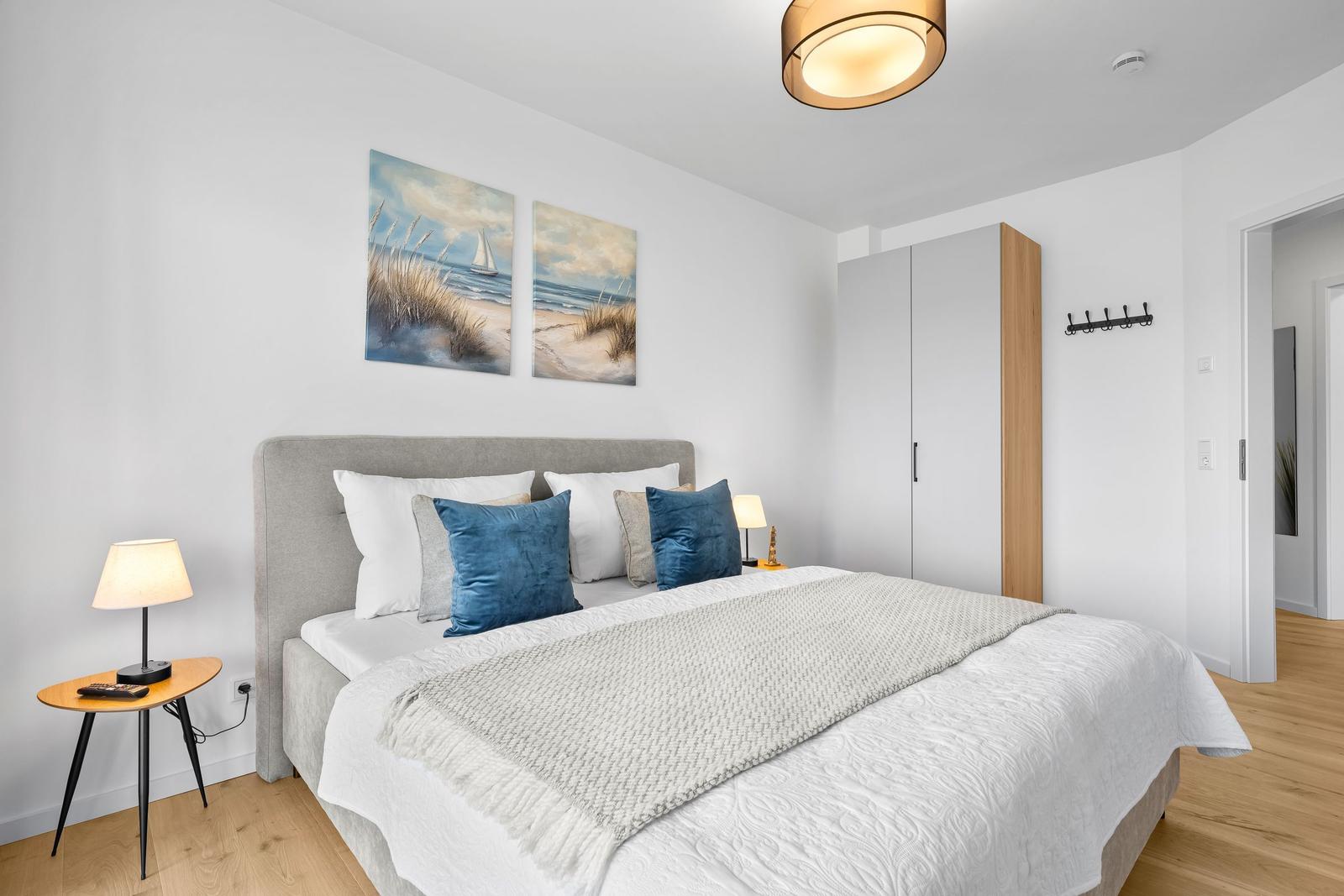 Schlafzimmer mit Bett, Nachttisch und Wandbildern. Holzboden und Kleiderschrank.