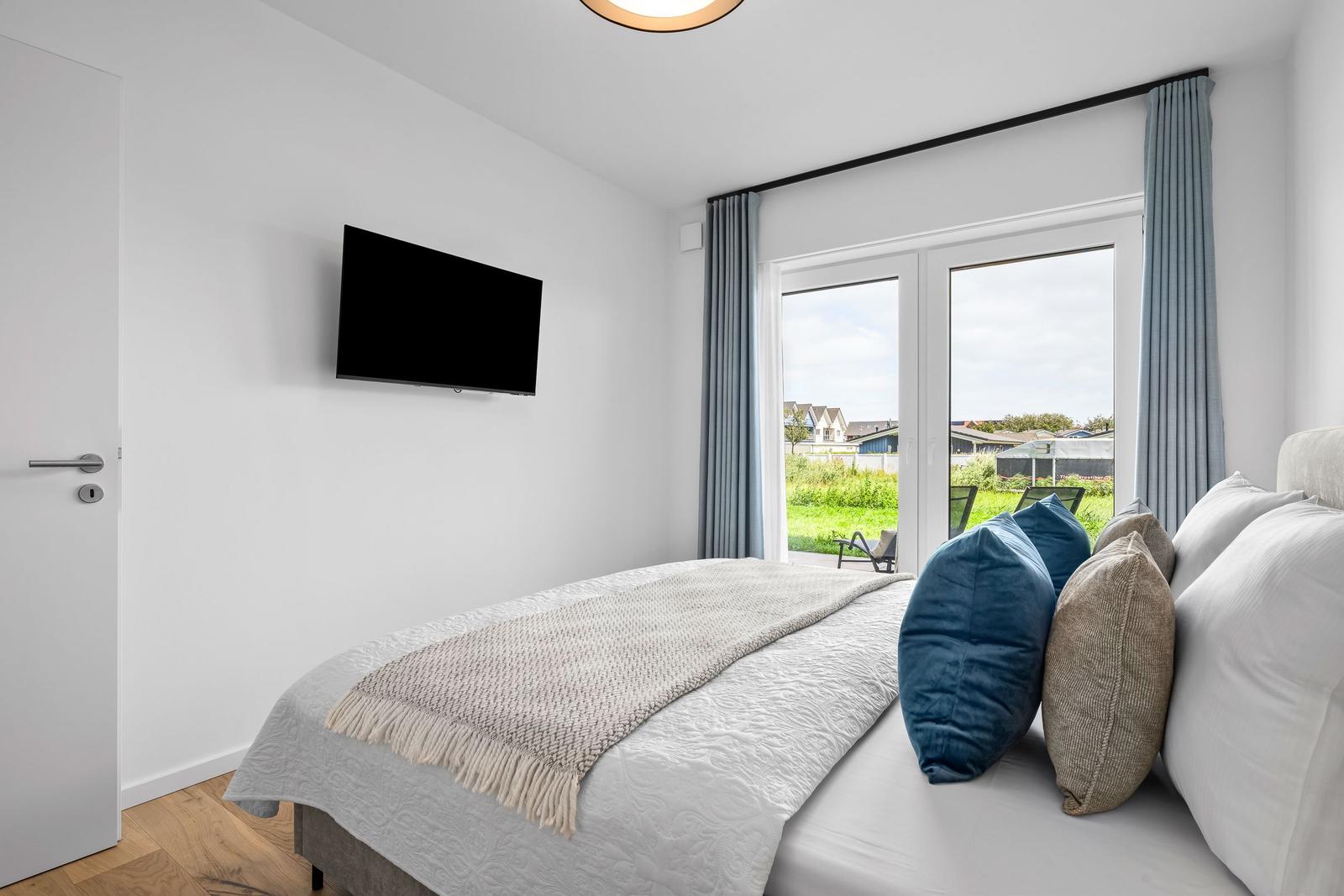 Schlafzimmer mit Bett, TV und Blick auf Garten.