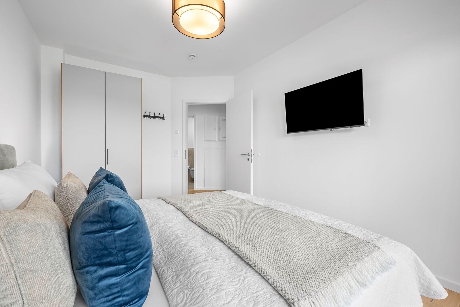 Schlafzimmer mit Bett, Kleiderschrank und Wandfernseher.