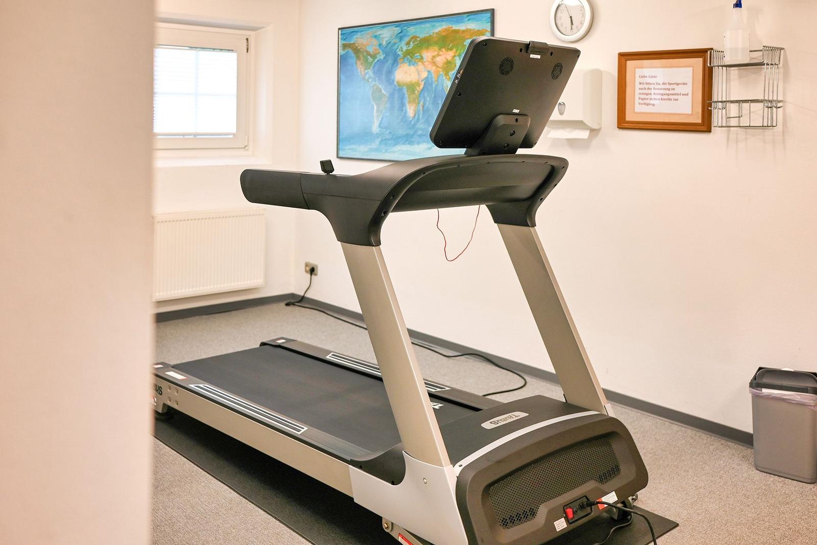 Laufband in einem Fitnessraum mit Weltkarte an der Wand und Fenster.