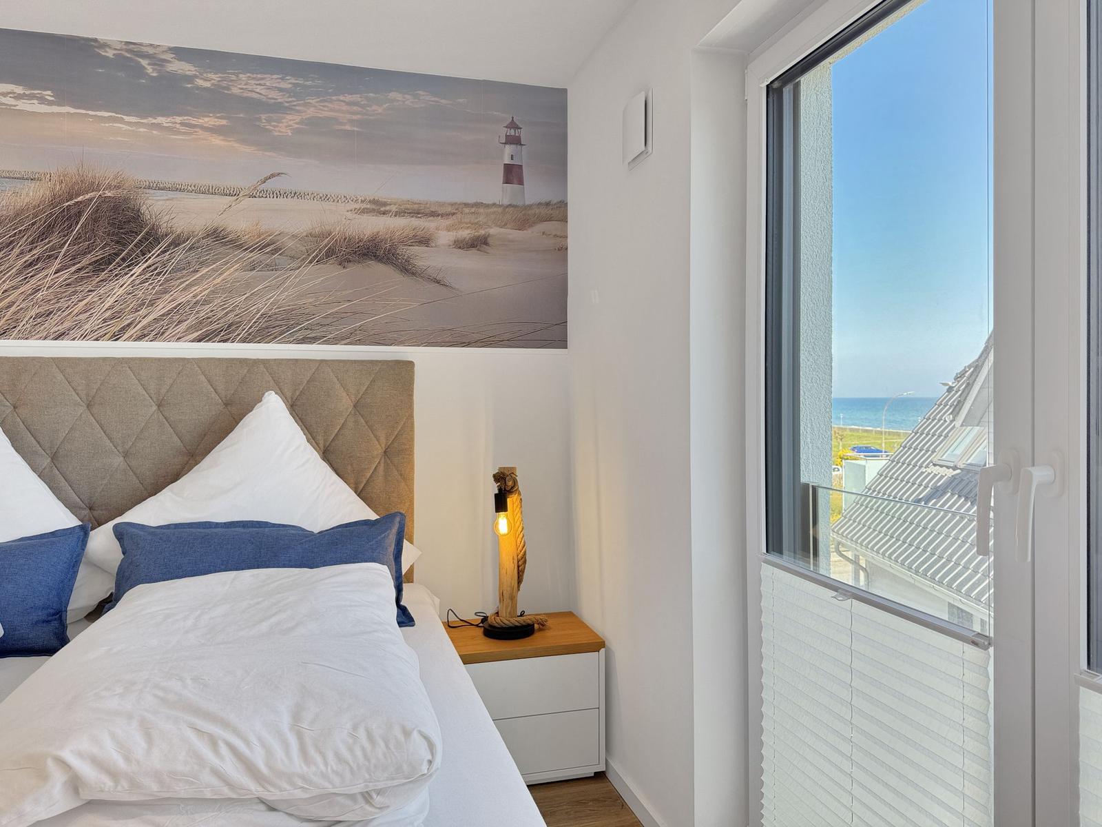 Schlafzimmer mit Blick aufs Meer und Leuchtturm-Bild an der Wand.