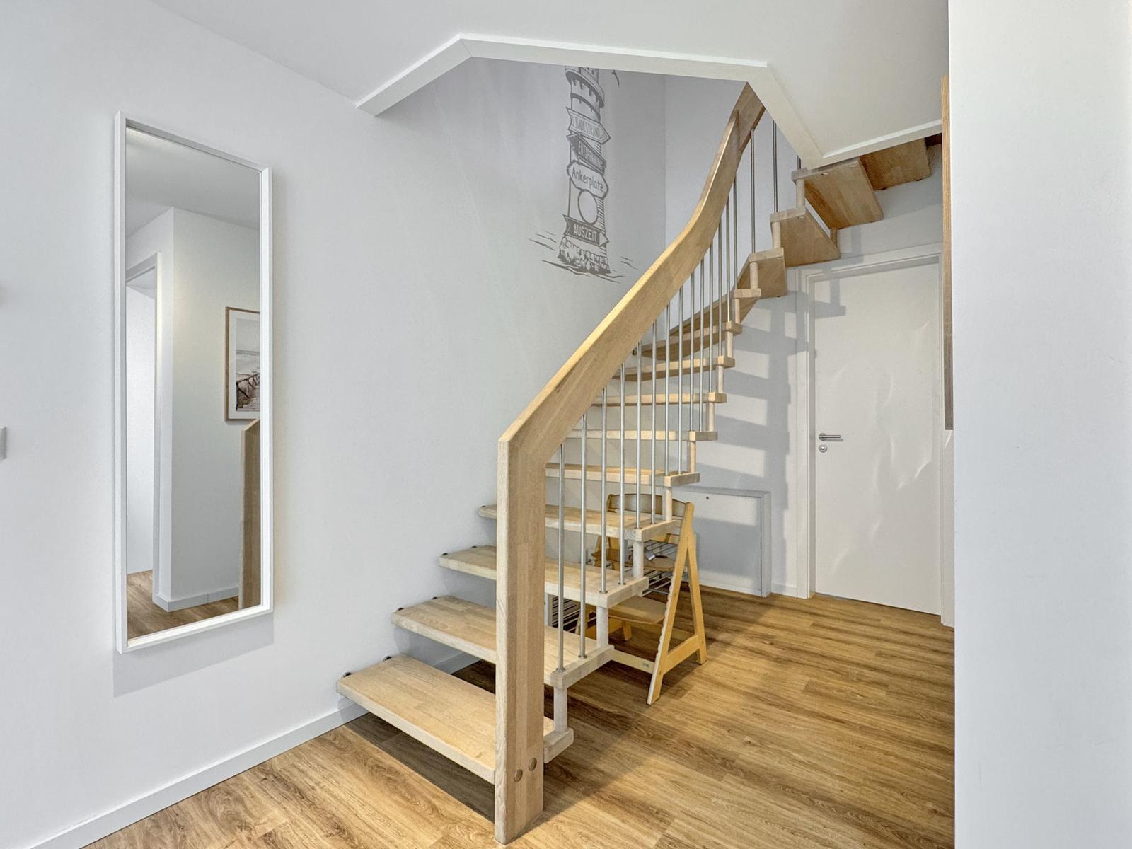 Holztreppe mit Metallgeländer führt zur oberen Etage. Wand mit Leuchtturm-Motiv. Spiegel an der Wand.