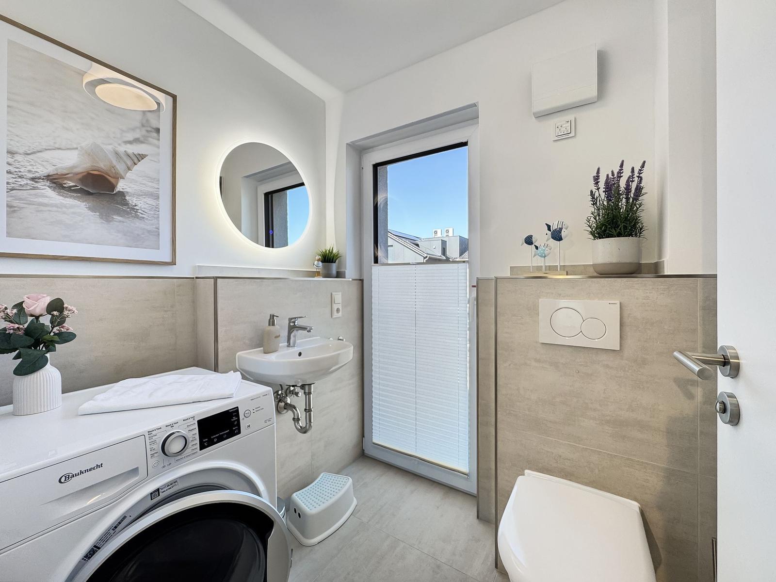 Badezimmer mit Waschmaschine, Spiegel und Fenster