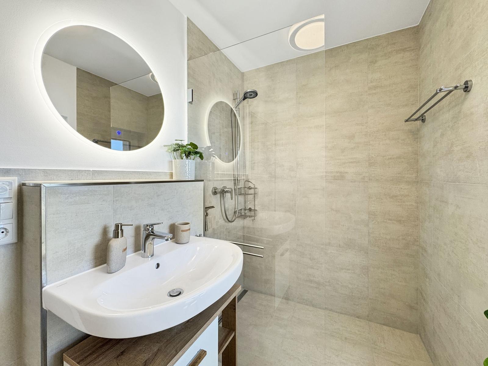 Badezimmer mit Dusche, Waschbecken und runden Spiegel