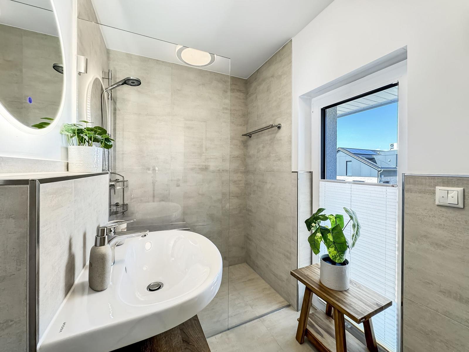 Badezimmer mit Dusche, Waschbecken und Fenster mit Pflanzen