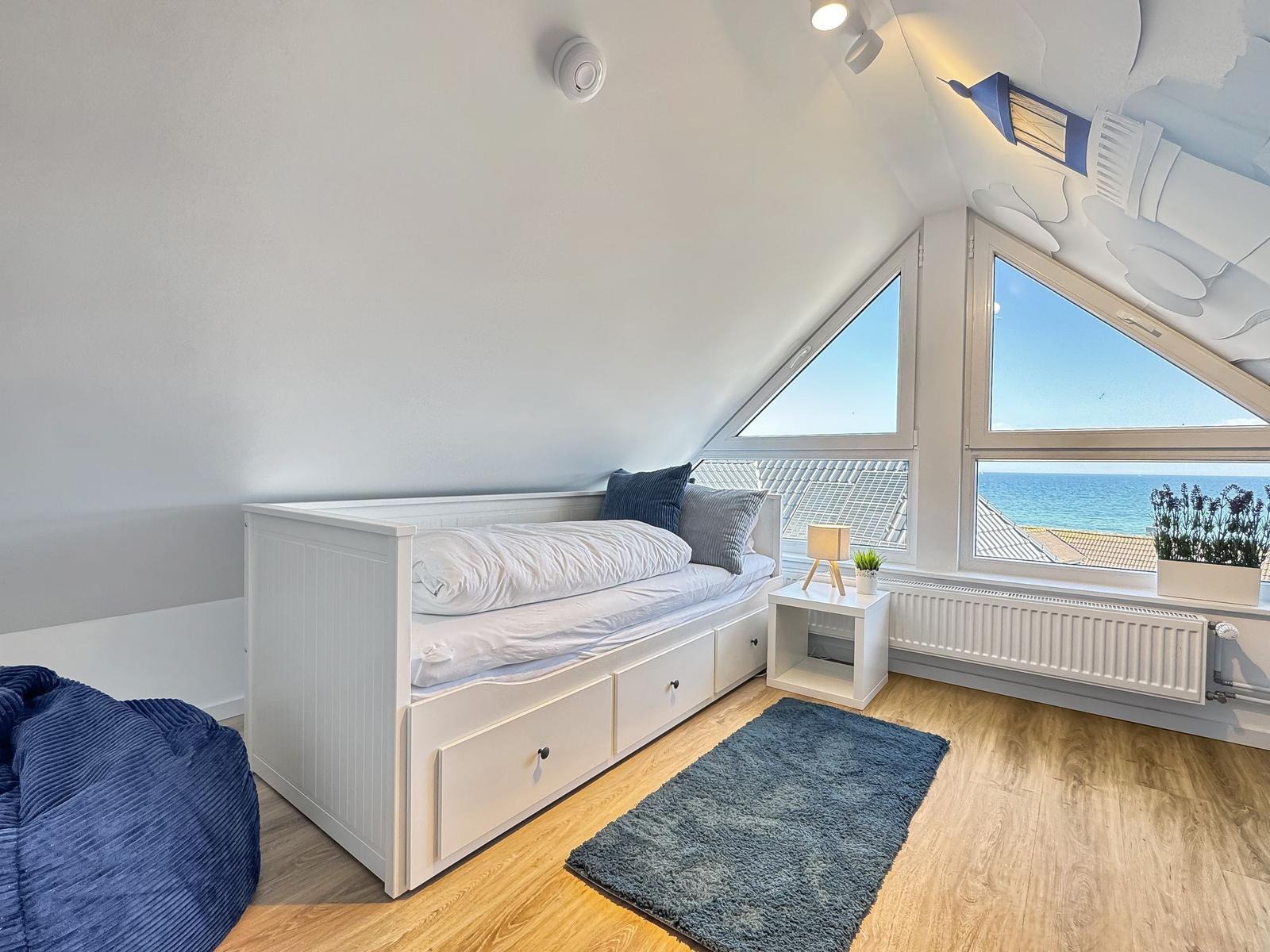 Schlafzimmer mit Blick aufs Meer, weißes Bett mit Schubladen, Holzboden und Fenster