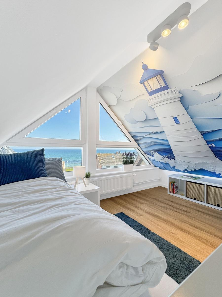 Schlafzimmer mit Blick aufs Meer und Leuchtturm-Wandbild.