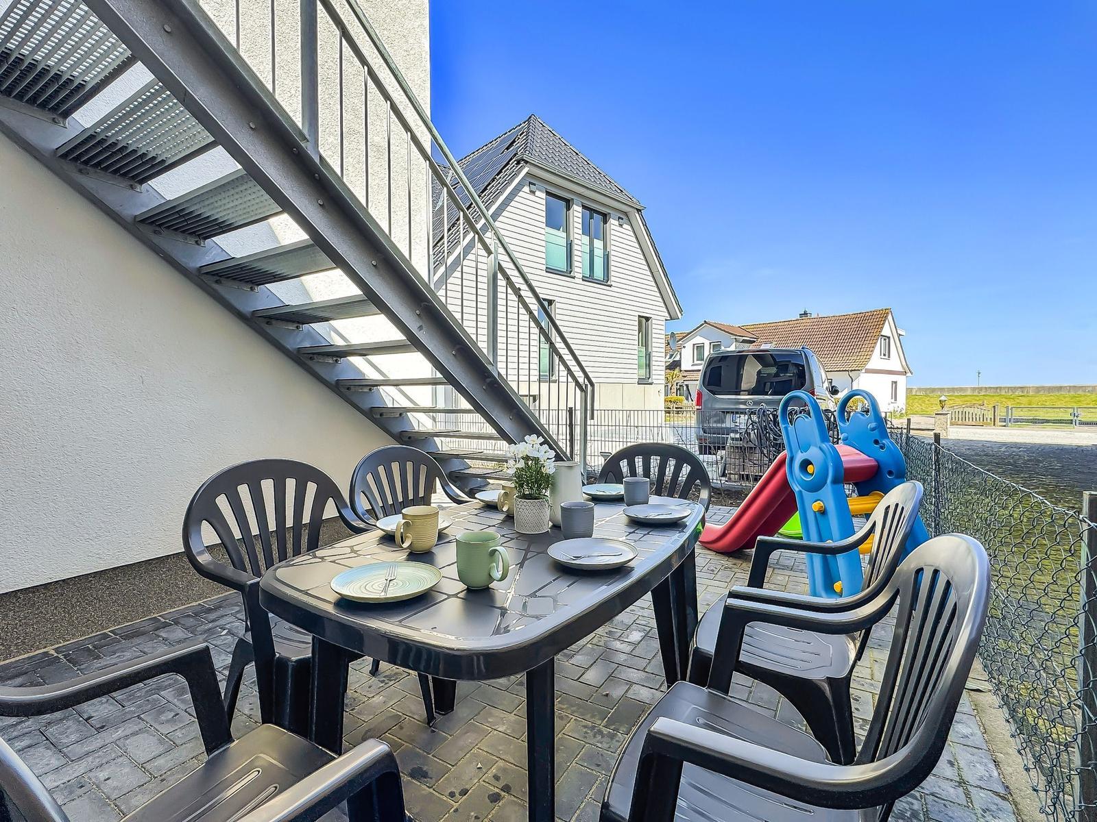 Terrasse mit Tisch und Stühlen, Spielplatz und Haus im Hintergrund.