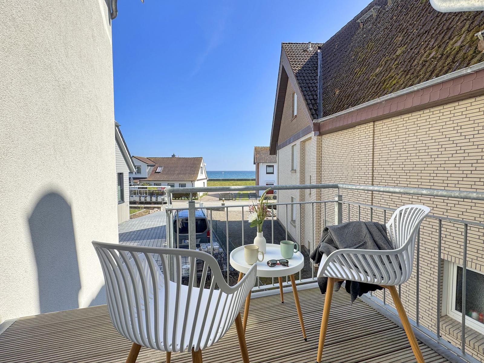 Balcony with two white chairs and a small table overlooking the sea.