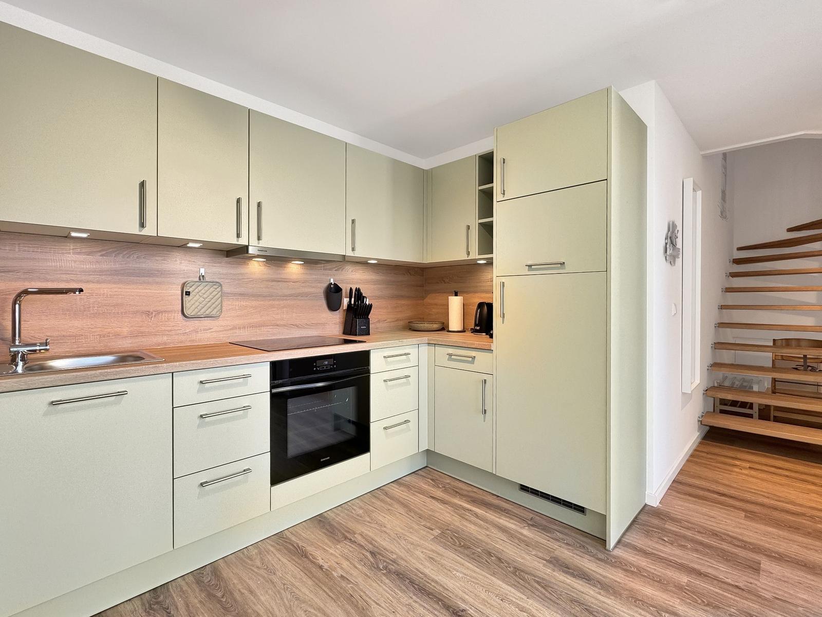 Moderne Küche mit Holzoptik und integriertem Backofen. Holzstufen führen in den Aufgang.