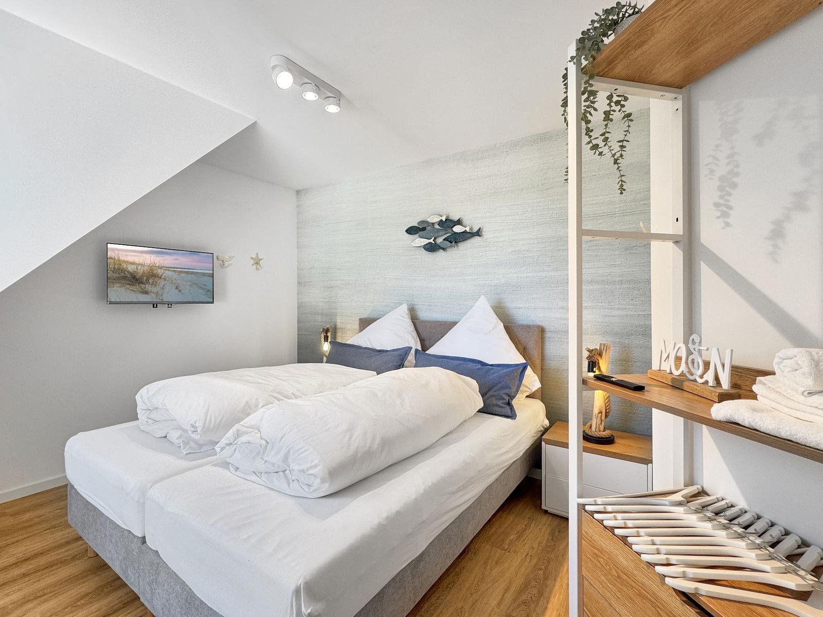 Schlafzimmer mit Doppelbett, Wand-TV und Holzmöbel. Decke geneigt, Wanddekoration mit Fischmotiv.