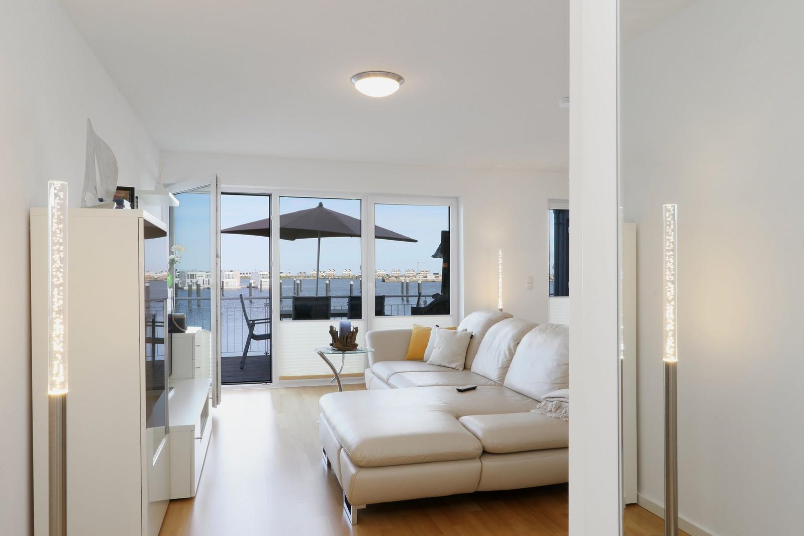 Wohnzimmer mit weißem Sofa und Blick auf den Hafen. Terrasse mit Sonnenschirm.