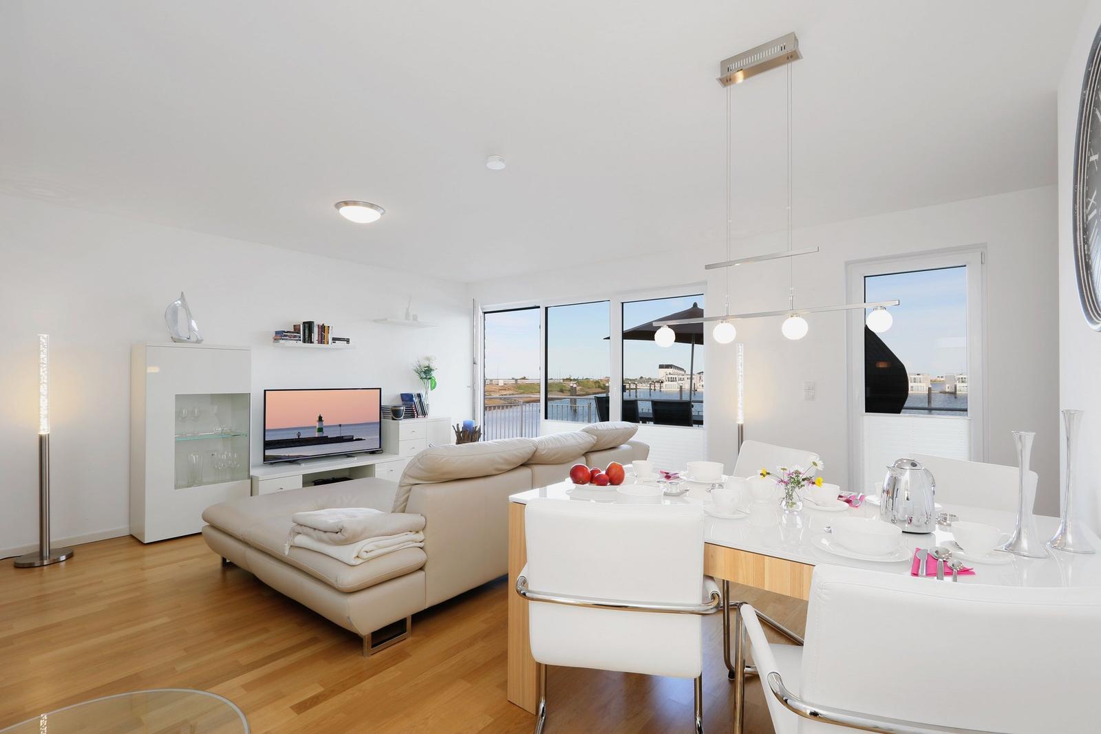 Wohn- und Essbereich mit Blick auf Wasser, weißer Sofa, Esstisch mit Stühlen und TV.