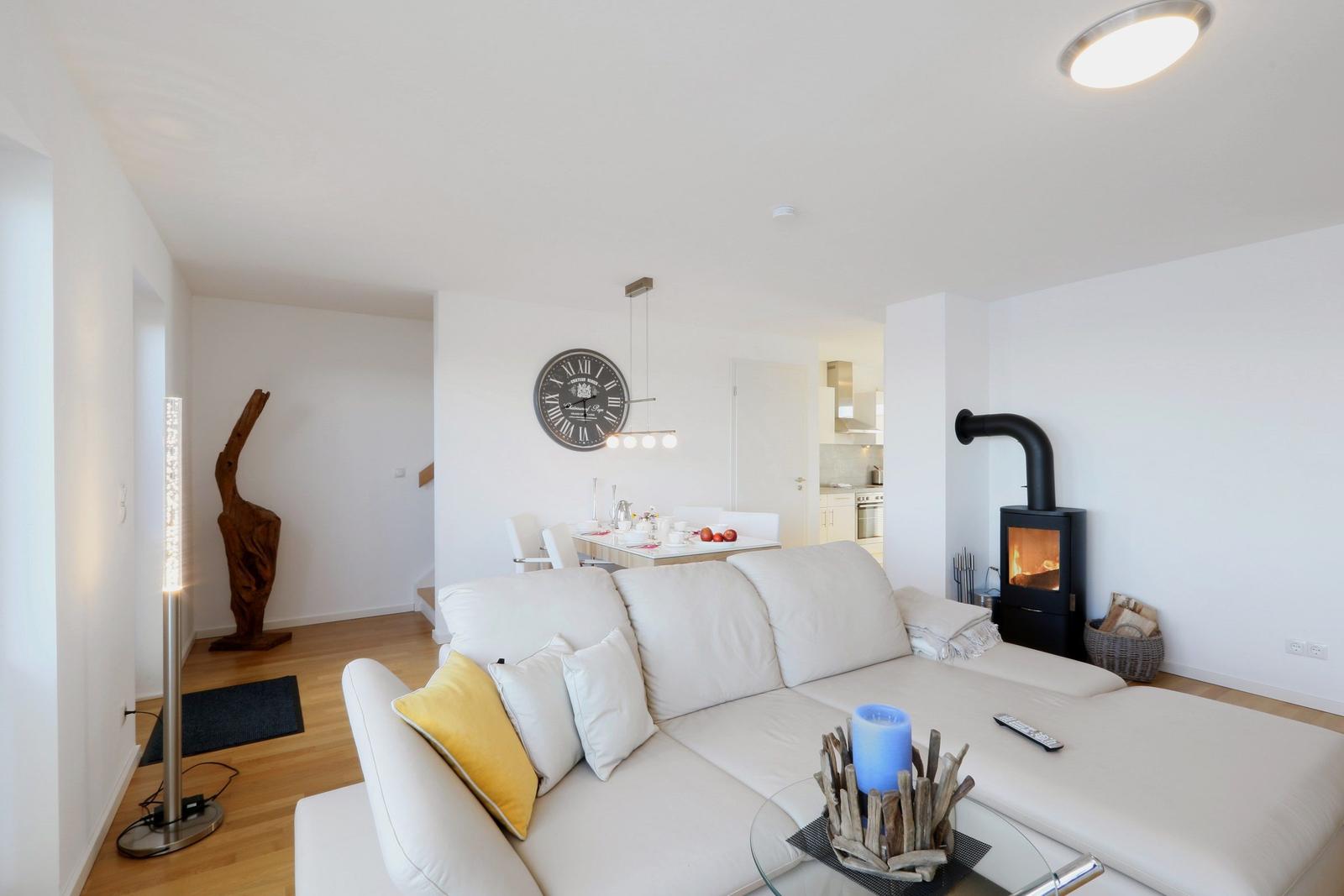 Wohnbereich mit Sofa, Kamin und Esstisch im Hintergrund.
