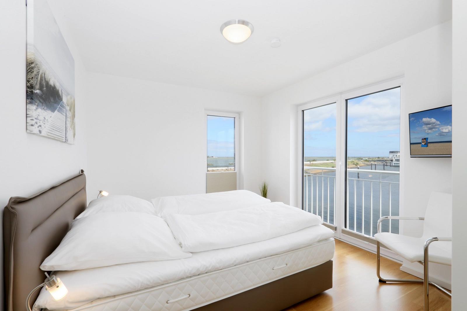 Schlafzimmer mit Blick auf Wasser und Balkon. Bett, Sessel und Fenster sind sichtbar.